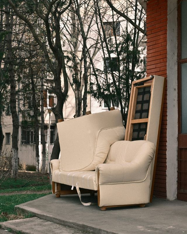 Een oude zetel en een fauteuil buiten tegen een bakstenen gevel, klaar om opgehaald te worden