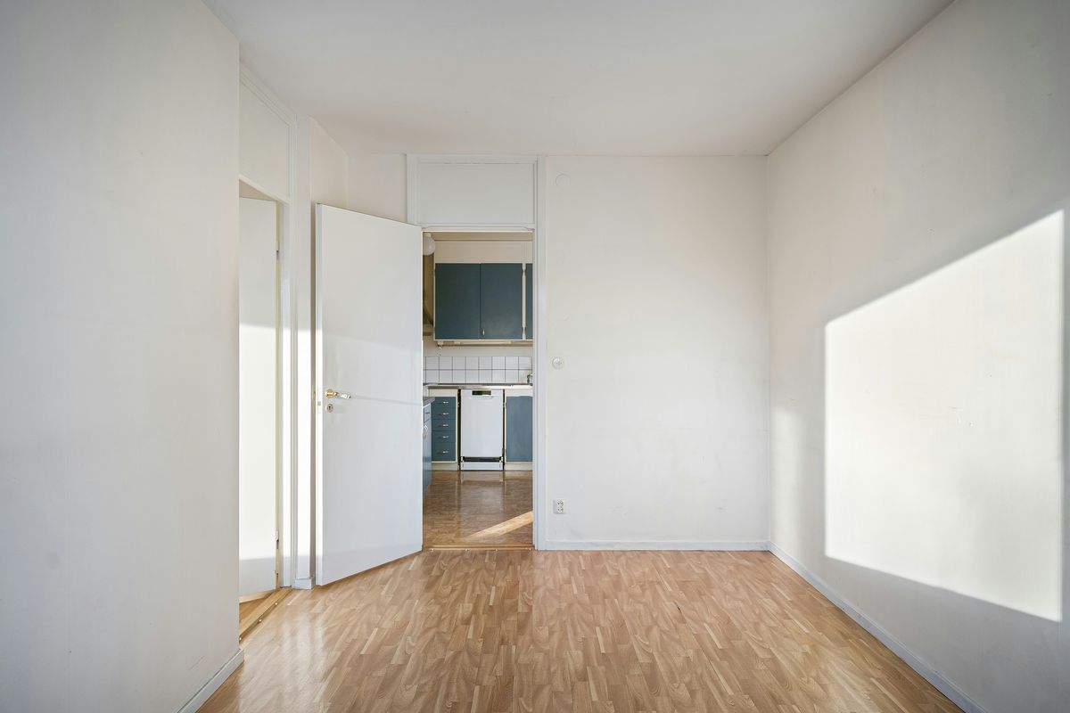 Lege, propere kamer met een parketvloer en een open deur naar de keuken